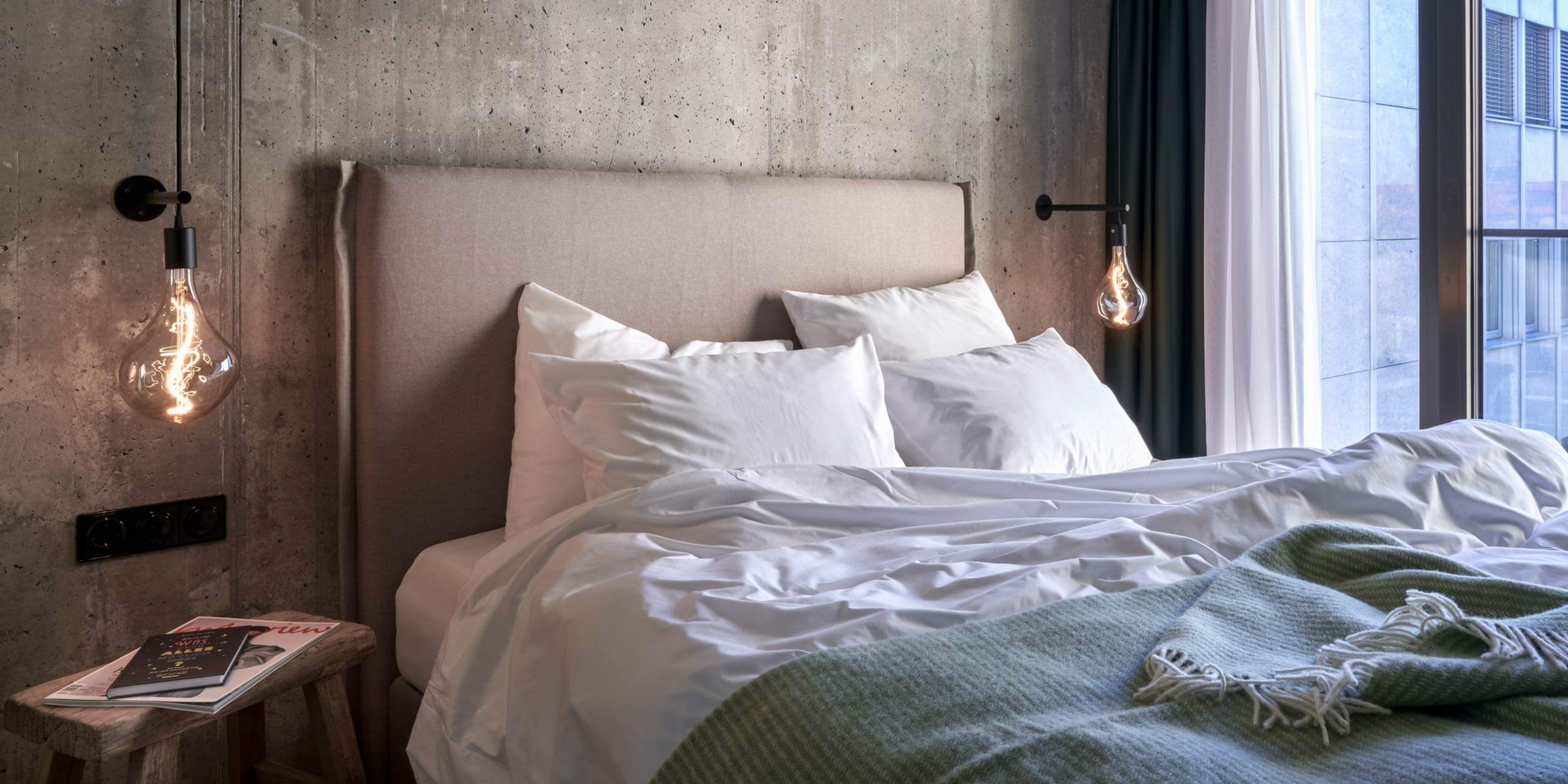 Superior Comfort Room: cozy bed with fabric head part in front of a concrete wall